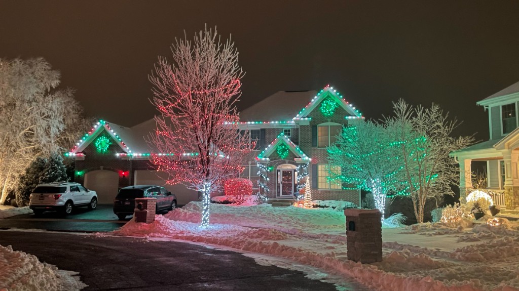 Snowy brick home with red and green tree wrap holiday lights